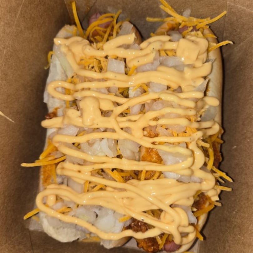 Two hot dogs topped with diced onions, shredded cheese, and a generous drizzle of cheese sauce.