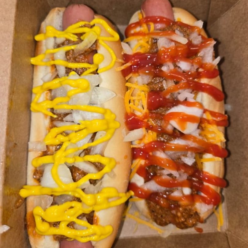 Two chili dogs, one with mustard and onions, the other with ketchup, cheese, and onions.