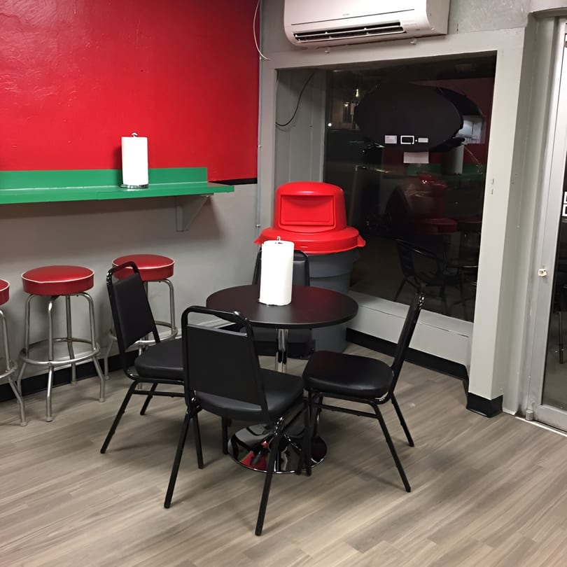 Interior of Sam's Hot Dog Stand with red walls, green shelf, black tables, and red bar stools.