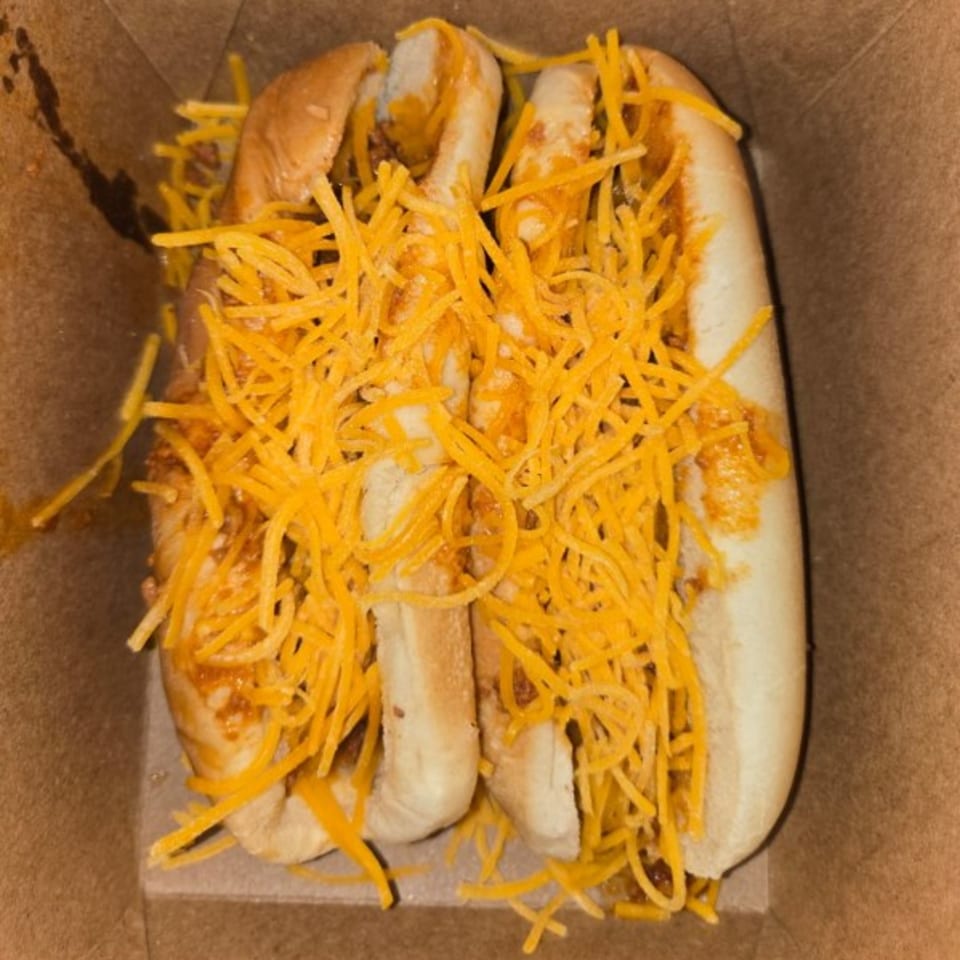 Two chili cheese hot dogs in a cardboard box, topped with shredded cheddar cheese.