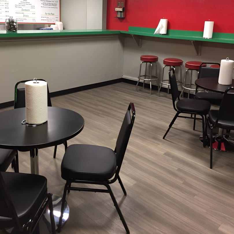 Interior of Sam's Hot Dog Stand with black tables, chairs, red stools, and a red and gray wall.