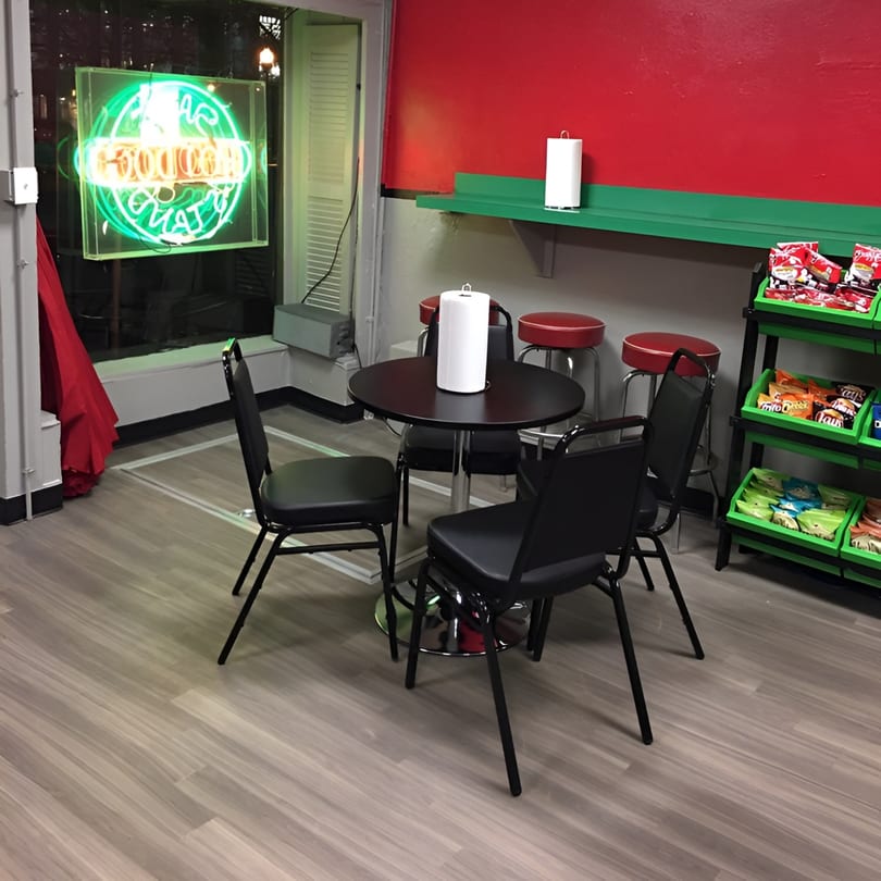 Interior of Sam's Hot Dog Stand with a black table, chairs, red bar stools, and a neon sign.